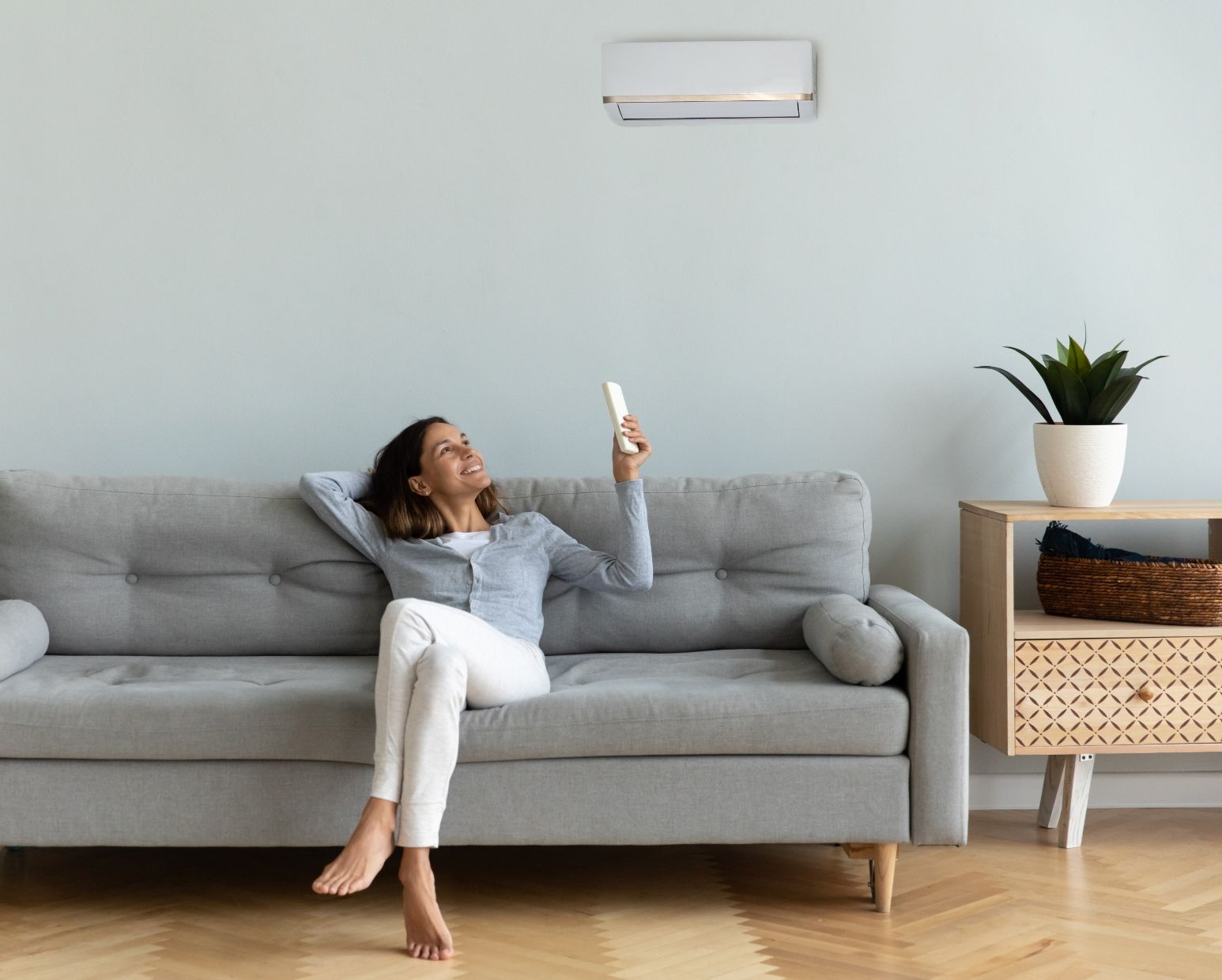 Eine Frau sitzt auf dem Sofa und schaltet die Klimaanlage ein